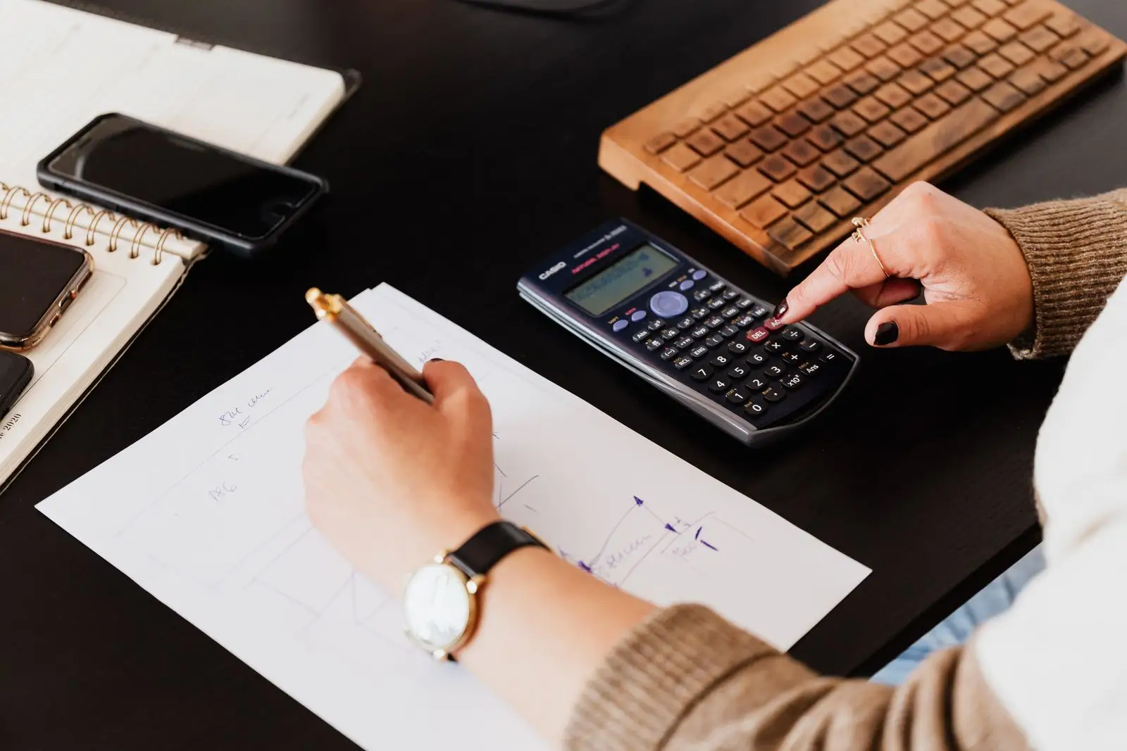 Persona haciendo cálculos con una calculadora y anotando cifras en una planilla de papel