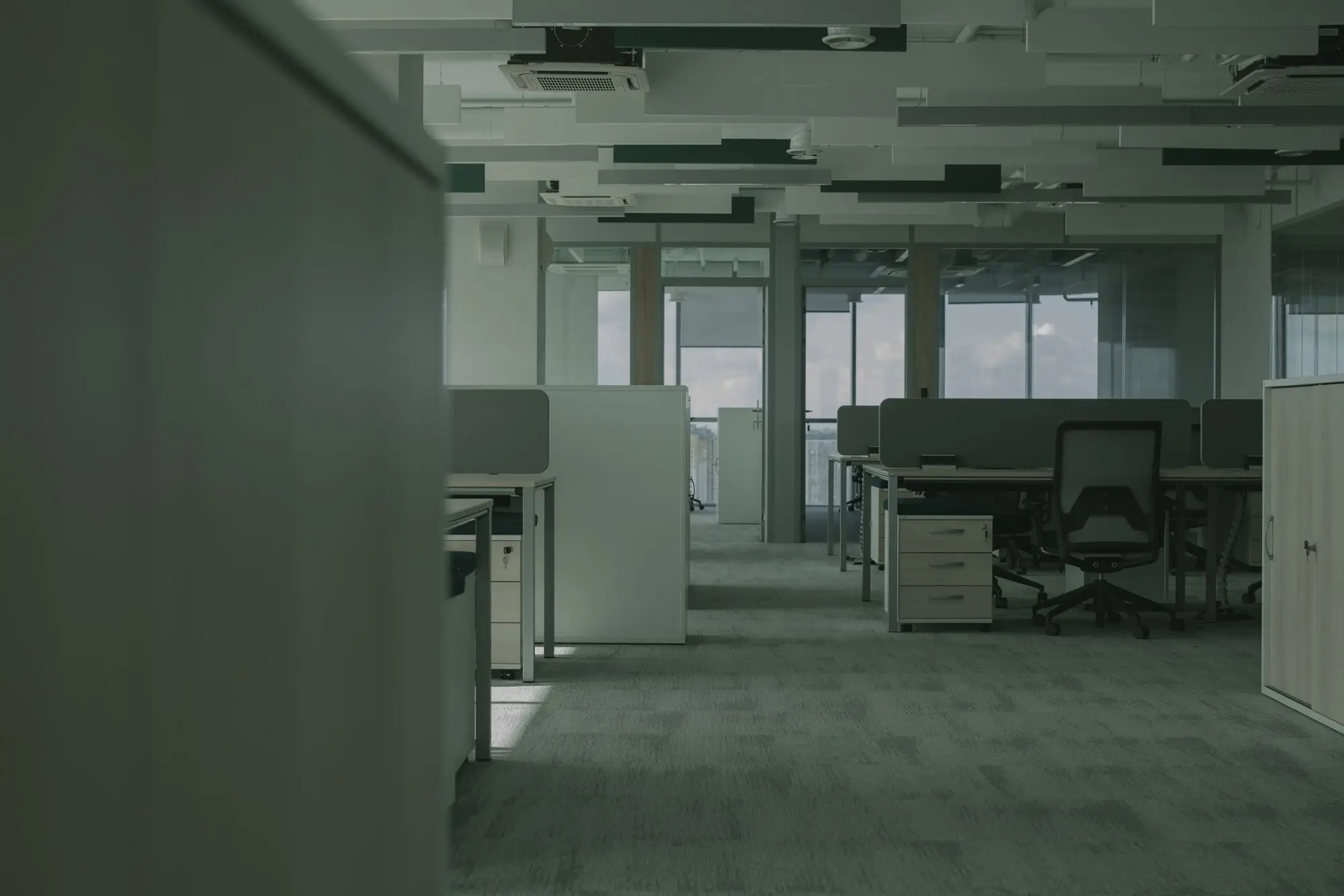 Oficina vacía en penumbra, con escritorios, sillas y cajoneras en su lugar y nadie trabajando