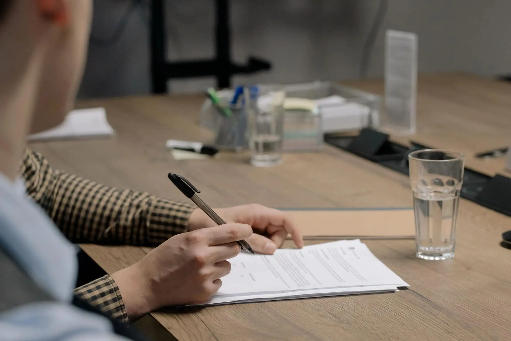 Persona firmando un documento sobre una mesa de madera en una oficina