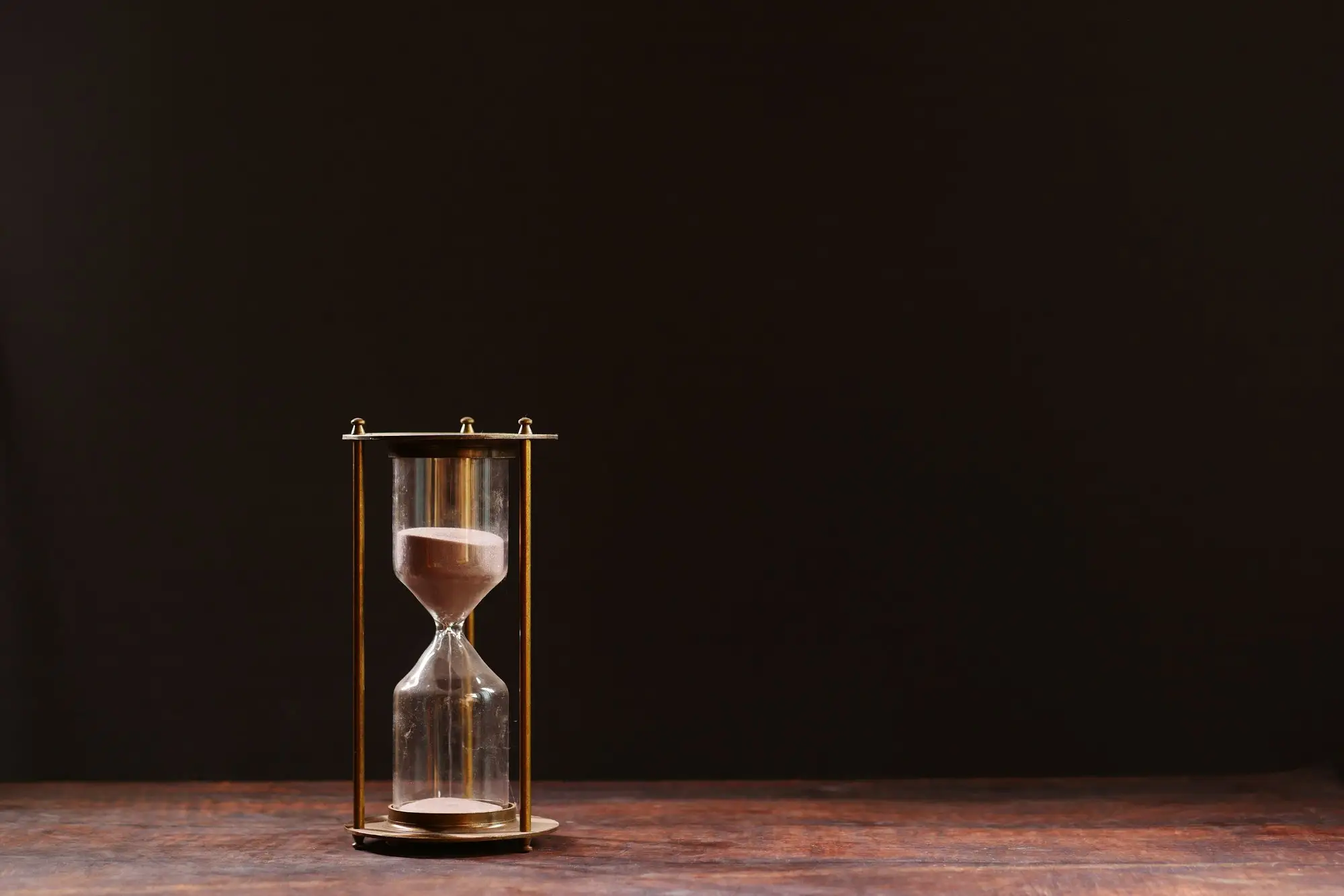 Reloj de arena de bronce sobre una mesa de madera oscura, con casi toda la arena todavía en la ampolleta superior